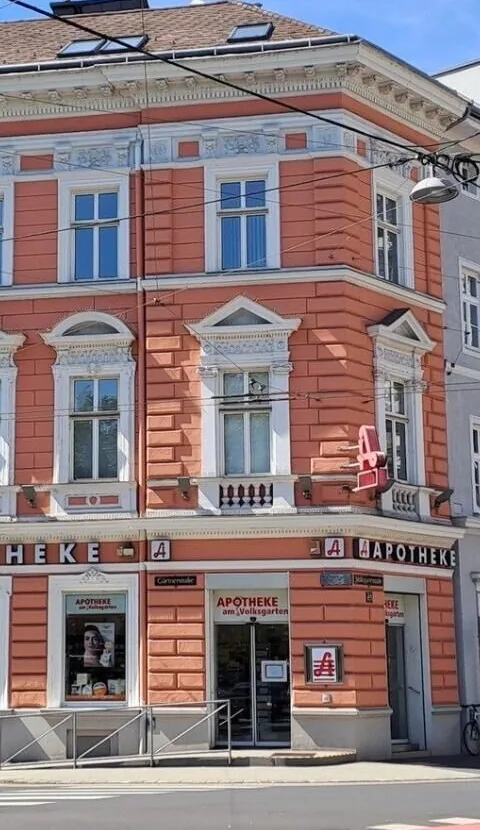 Eckhaus der Apotheke am Volksgarten mit Eingang, Schriftzug „Apotheke am Volksgarten“ und Apotheken-A