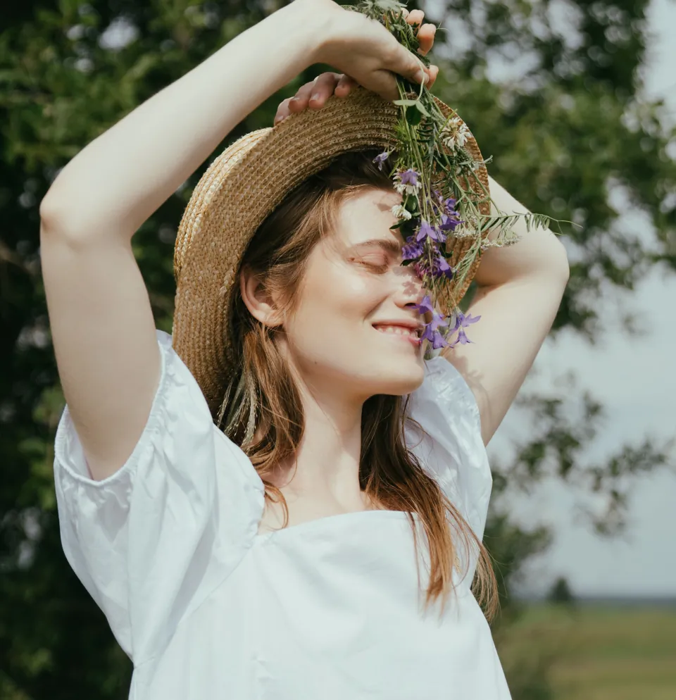 Lächelnde junge Frau mit Strohhut und Wiesenblumen in der Sonne