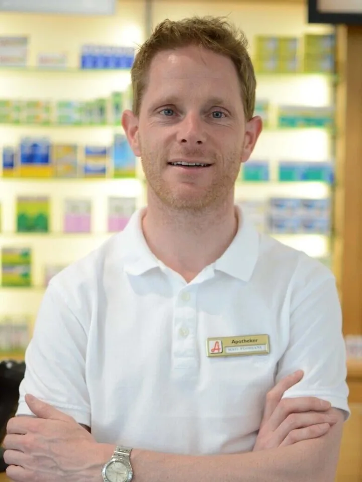 Porträt von Apotheker Mag. pharm. Stephan Floriani im weißen Poloshirt vor einem Regal in der Apotheke