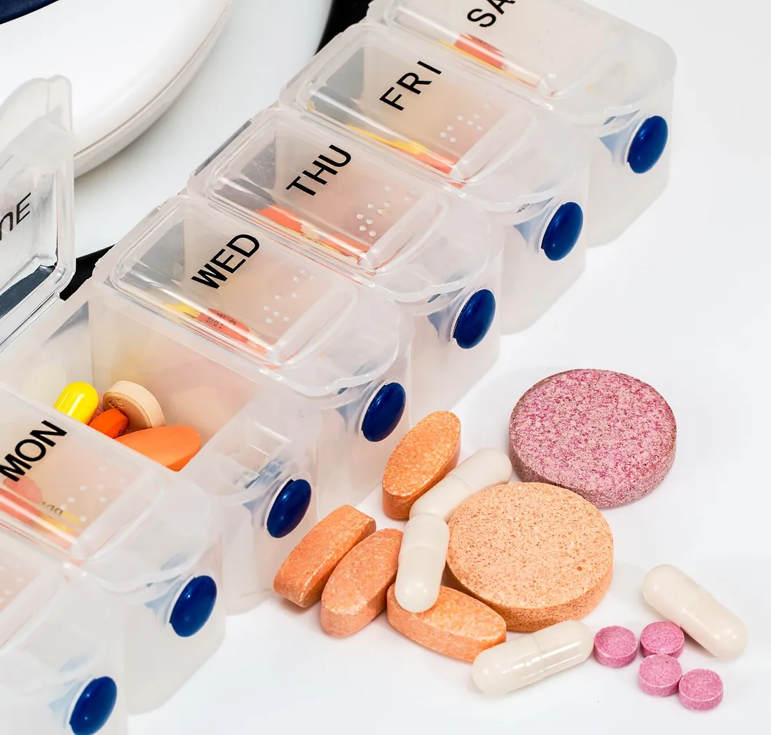 Tablettenbox mit Wochentagen, daneben Vitamin- und Brausetabletten
