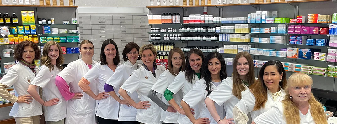 Das Apothekenteam in weißen Kitteln in einer Reihe vor den Regalen der Apotheke